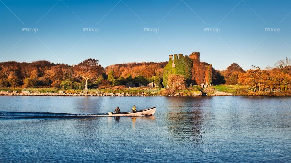 Menlo castle in fall colours by the Corrib River with boat passing by