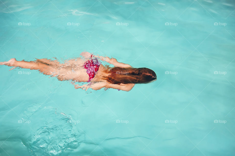 Young woman swimming and relaxing in swimming pool. Candid people, real moments, authentic situations