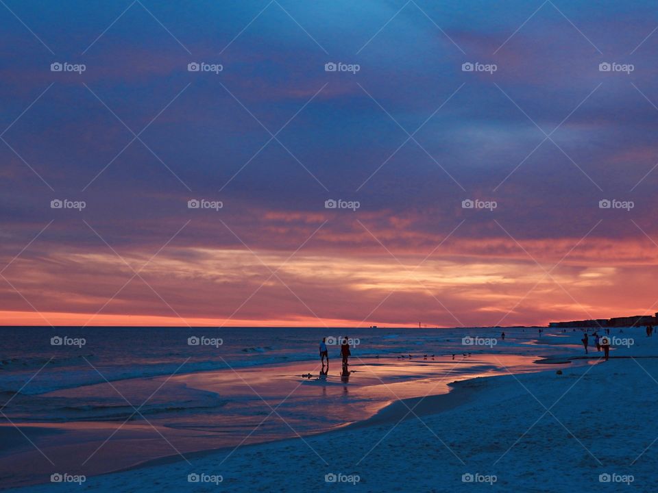 The Magical Outside - Magnificent Sunset - A couple walks on the sandy beach in front of the Gulf of Mexico at sunset. The descending sunset reflects on the water