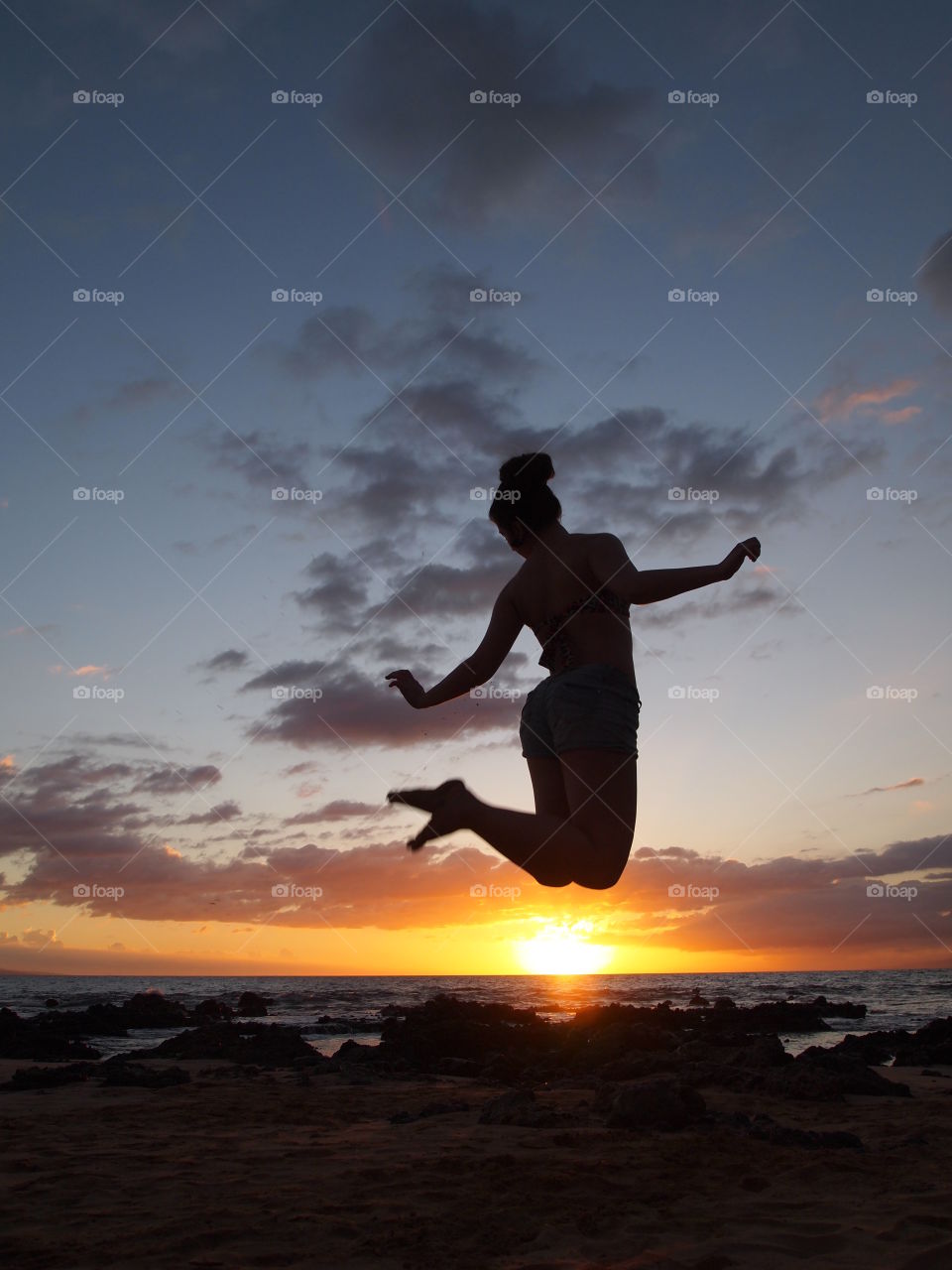 Silhouette of girl in mid air at the beach during sunset.  