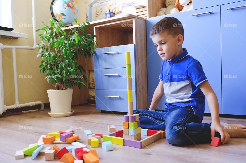 A little boy, a schoolboy, plays with wooden cubes at home, collects a constructor.