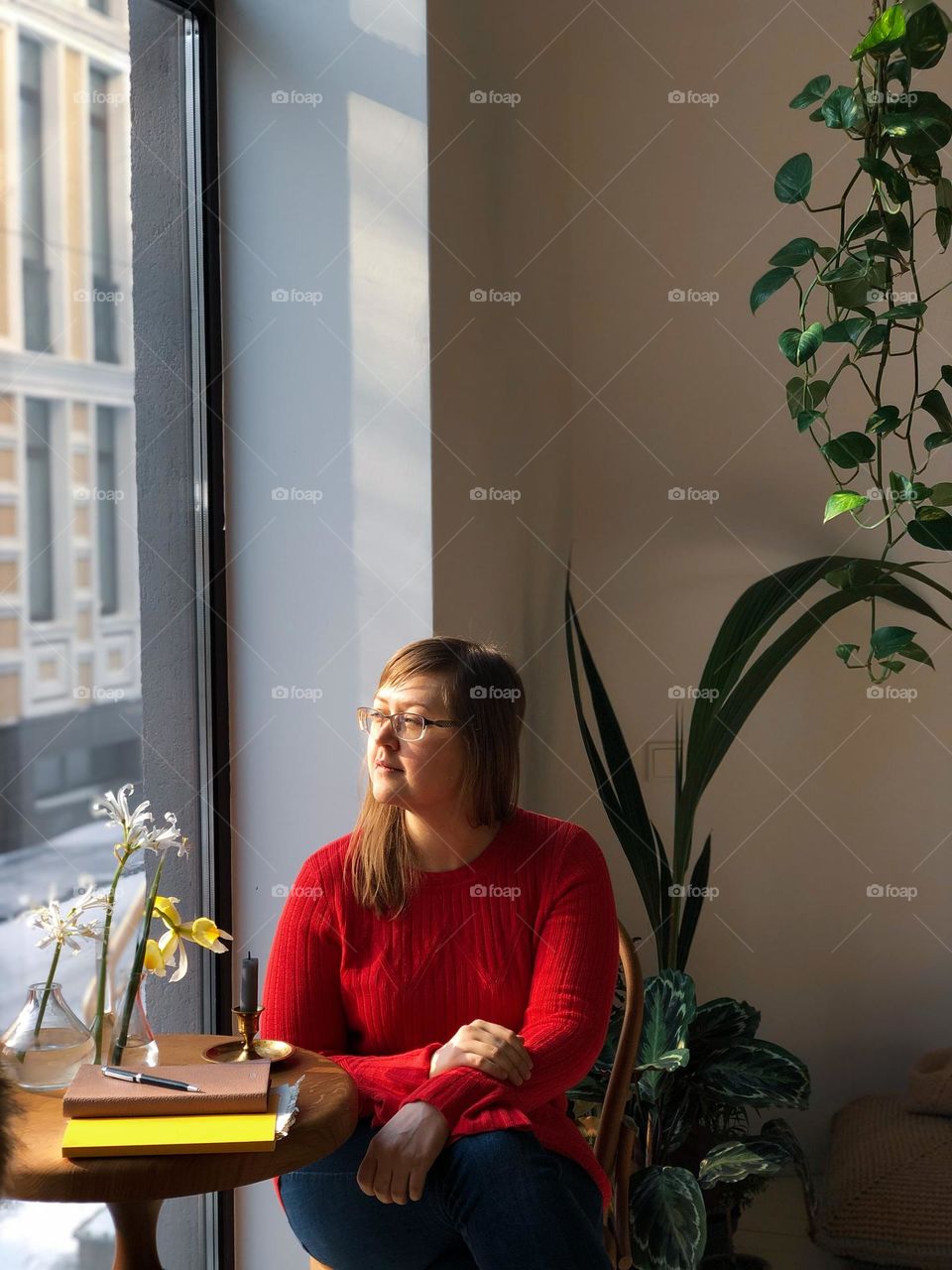 Woman in a red sweater sits near a table and flowers 