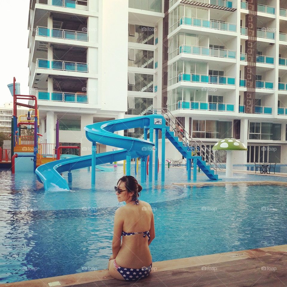 Asian woman in bikini sitting at pool.