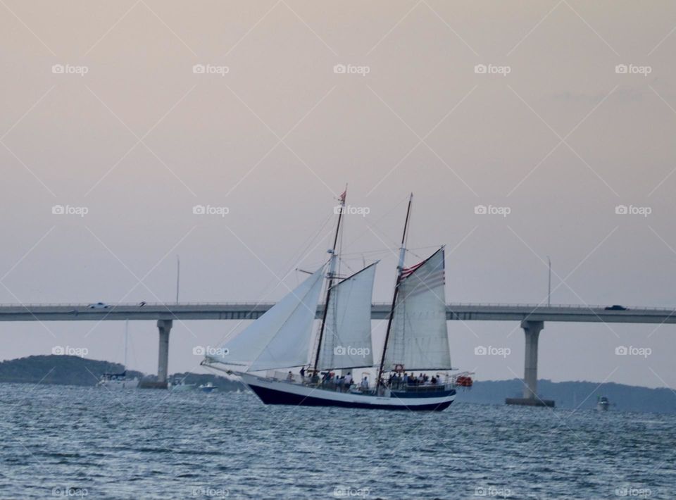 A large sailboat in front of a bridge on a river at dusk
