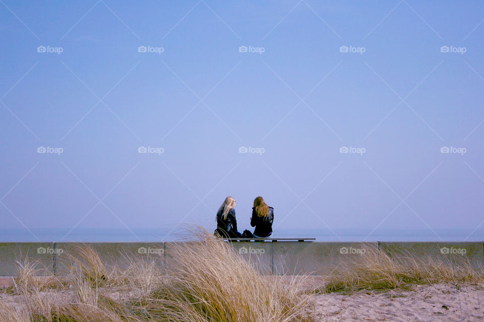 Zwei Mädchen sitzen auf einer Mauer an der Küste