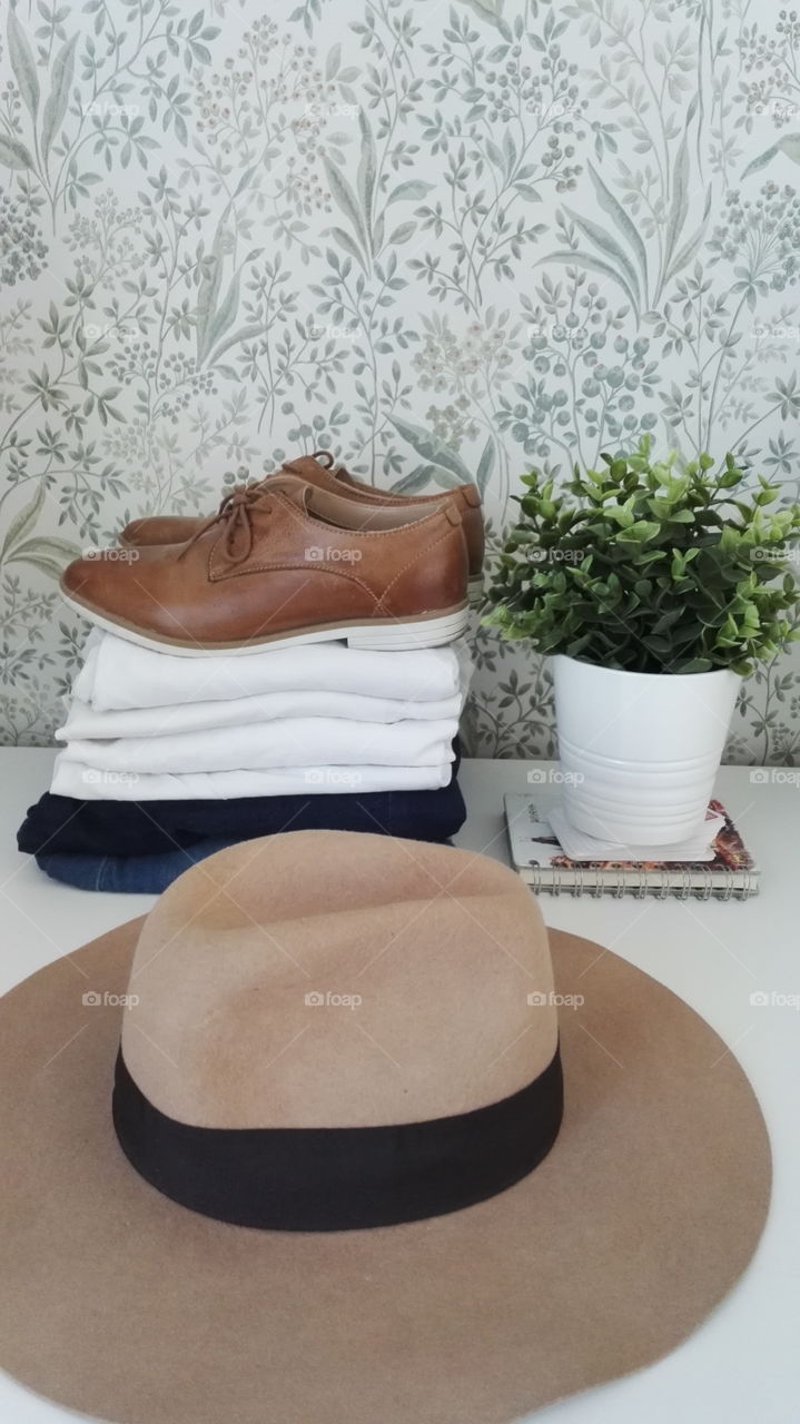 White t-shirts, jeans, plant and a hat on a white table. Lightful travelling happy casual.