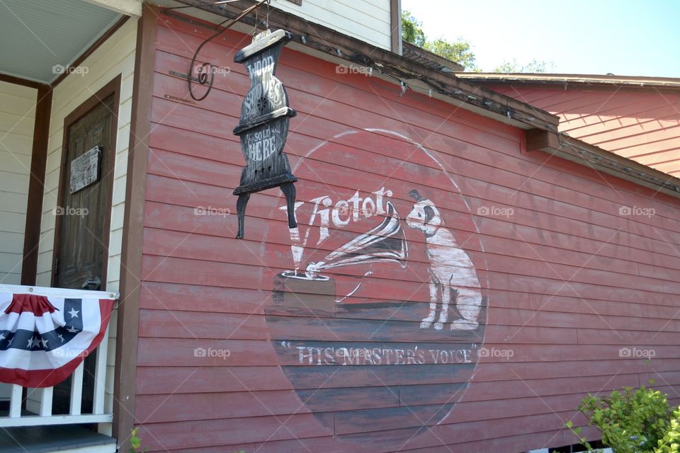 An old red wooden wall with a circular picture of a white dog and an antique phonograph and a hanging sign shaped like an iron pot-belly stove