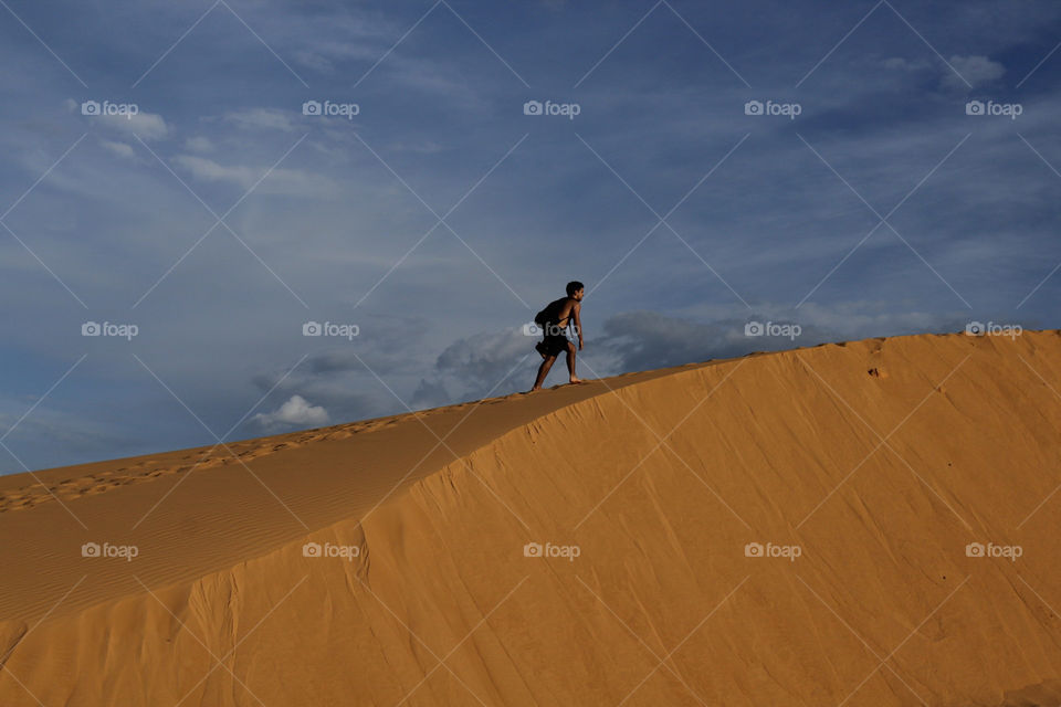 boy climbing a sand bank of Jalapão in Brazil in contrast with a blue beautiful sky