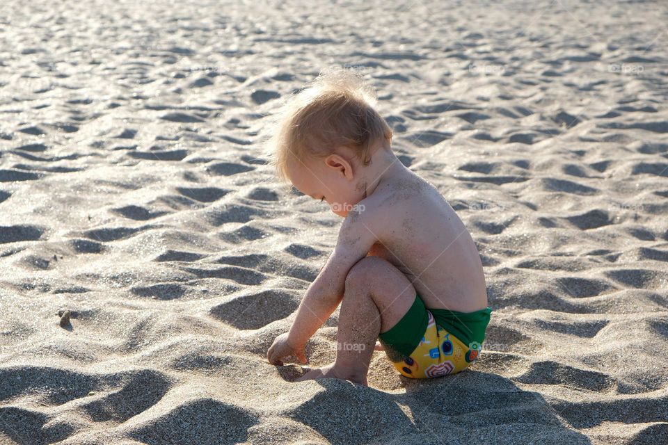 Little child sits on a sandy beach with his back to the viewer