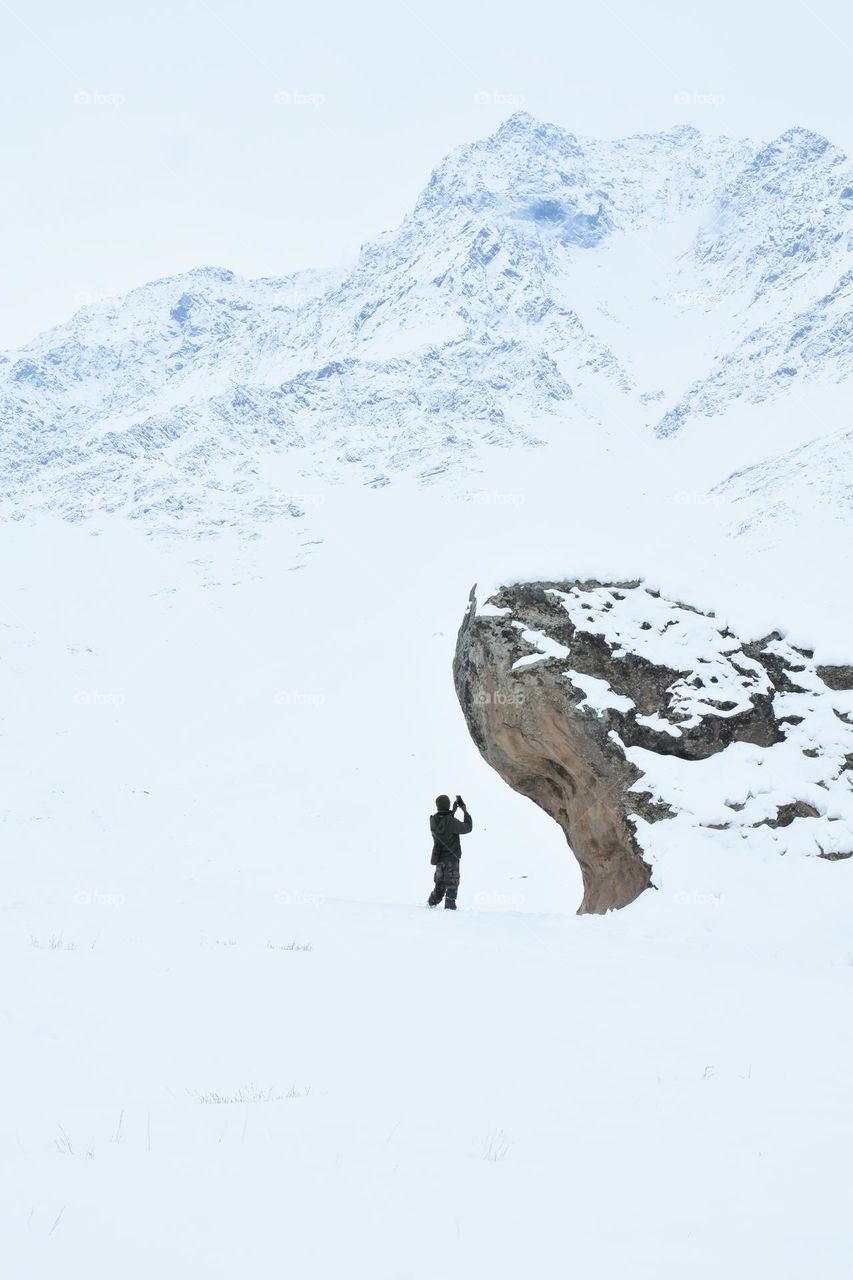 man taking image of snow covered mountain beside a big rock