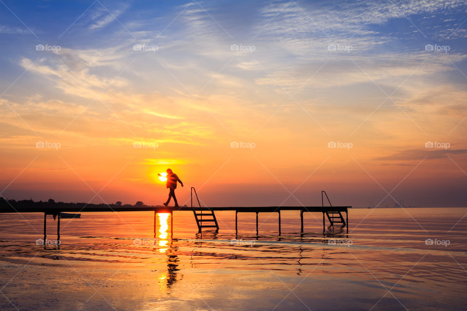 Silhouette walking on jetty at sunrise sunset 