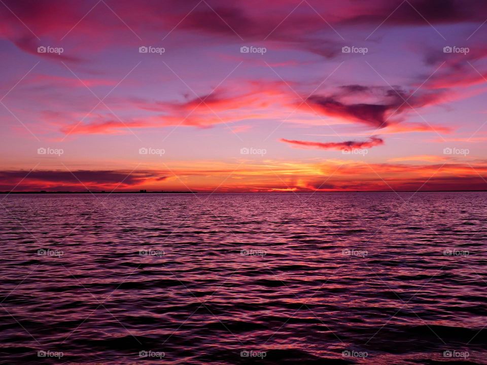 A mauve sunset scene over the Gulf of Mexico near Okaloosa County, Florida, with a person kayaking. The sky is filled with vibrant orange and purple hues, typical of sunsets during the "golden hour".