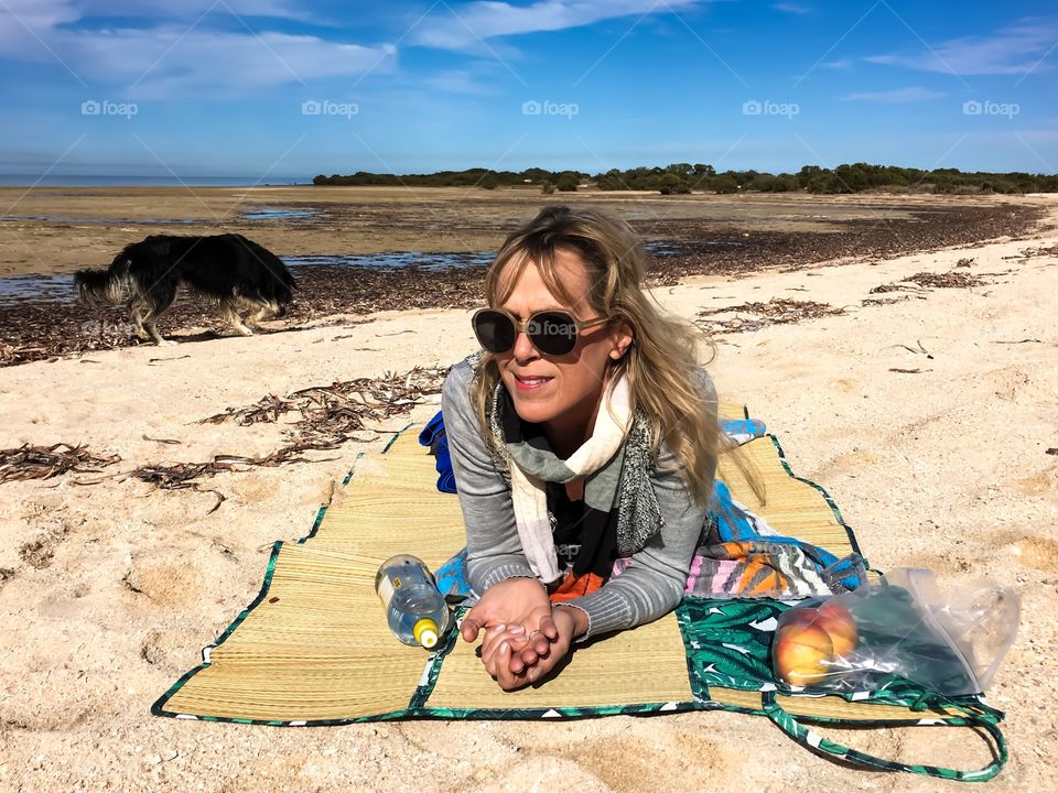 Woman laying on south Australia beach at low tide, border collie sheepdog in background 