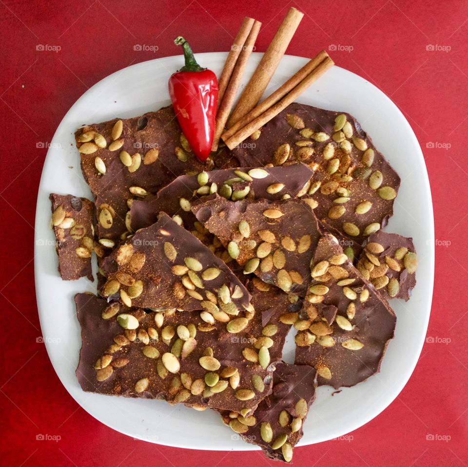 More Chocolate - Cinnamon Chocolate Chili Bark with cinnamon sticks and red chili pepper on a white plate, red background 