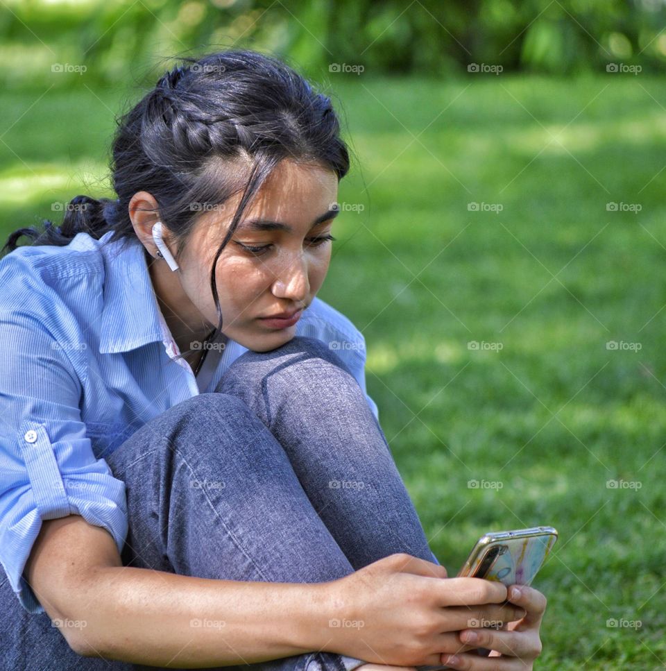 girl looking at a smartphone while sitting on the lawn