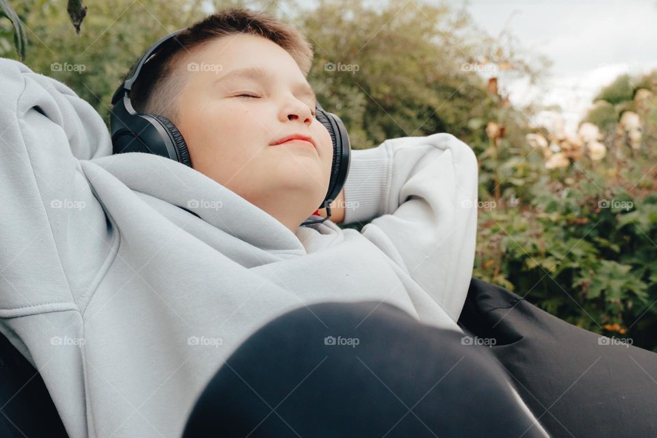 Teen smiling happy boy Gen z listening to music online on phone in earphones relaxing outside 