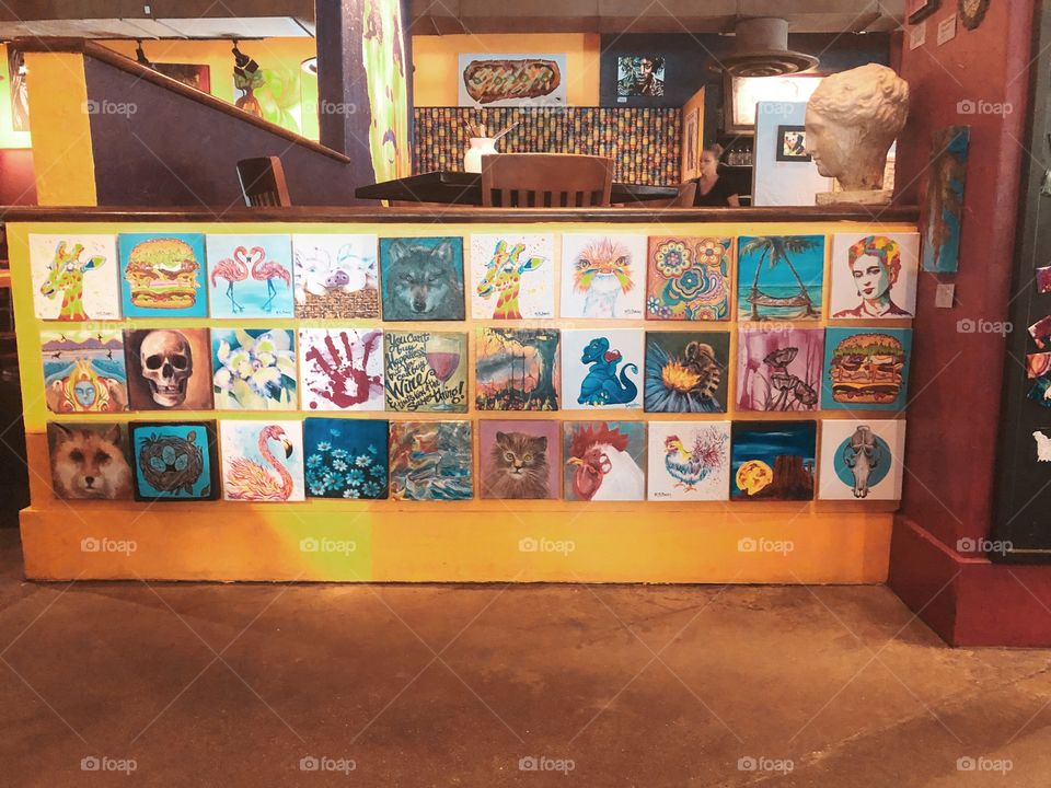 An array of magical and colorful works of art displayed in a cozy small town cafe. 
