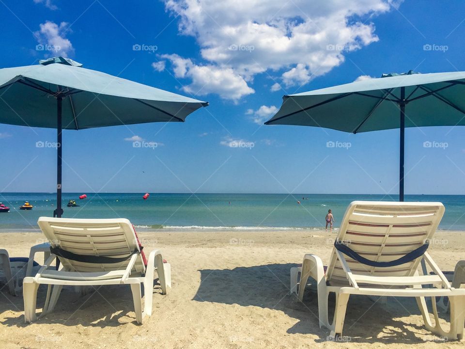 Two empty sunbeds with umbrellas on a sunny day at the beach