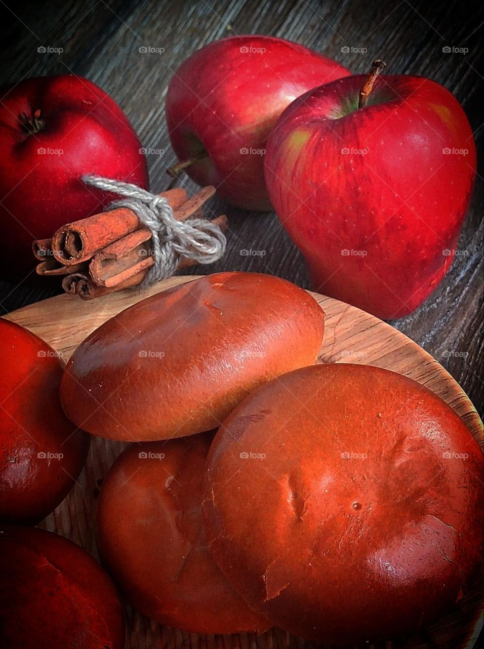 Food. On a wooden plate are pies with apple filling and cinnamon. Next to the plate are cinnamon sticks tied with a rope and red apples.