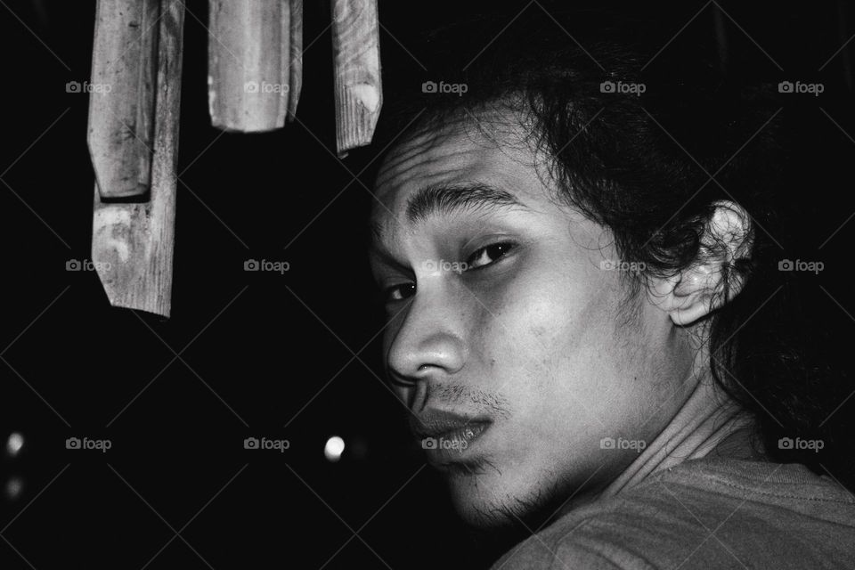 Close up black and white portrait of an Asian man with a sharp gaze looking behind him, dark background.