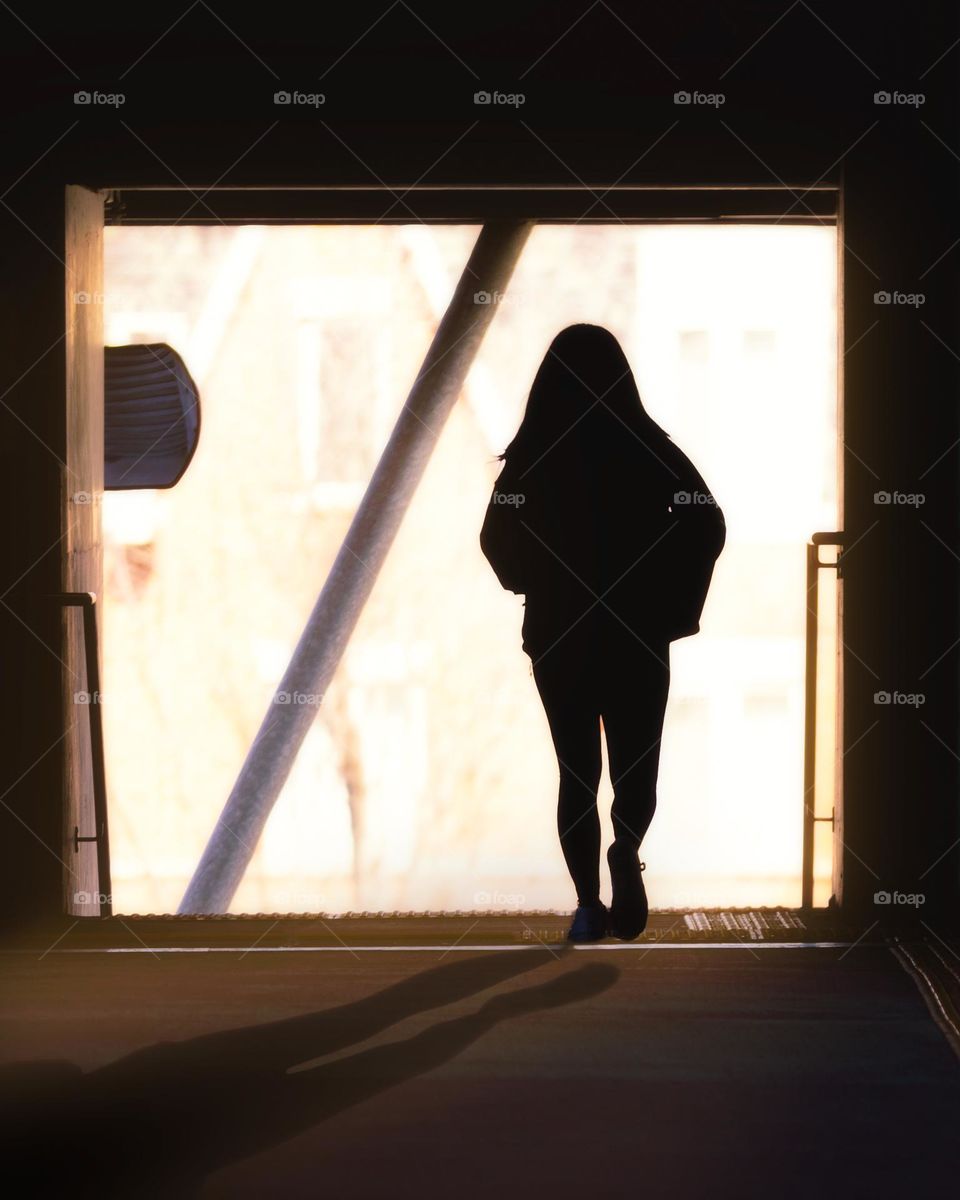 Silhouette of a woman walking towards a big open window entranceway with sunlight streaming in