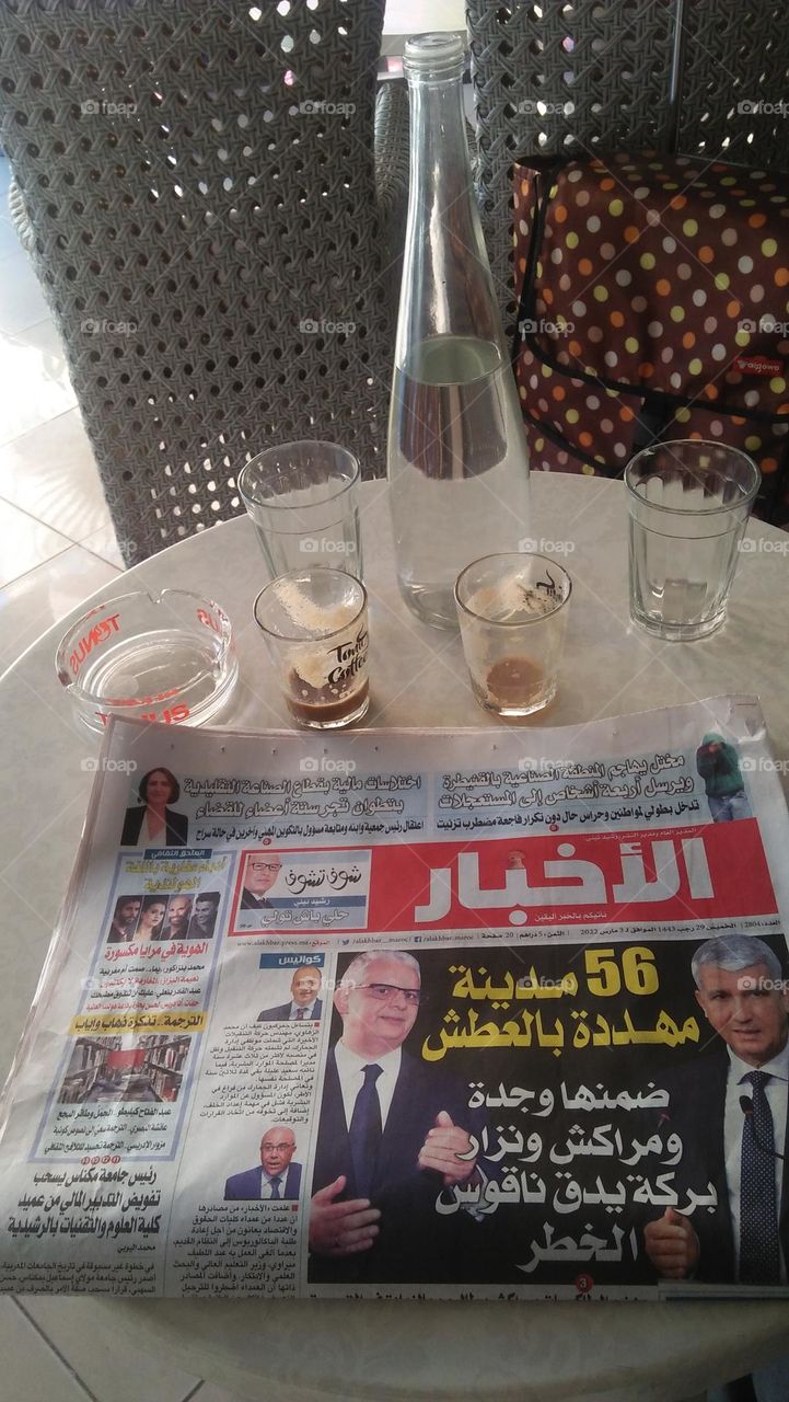 on table a bottle.  cups and a newspaper.