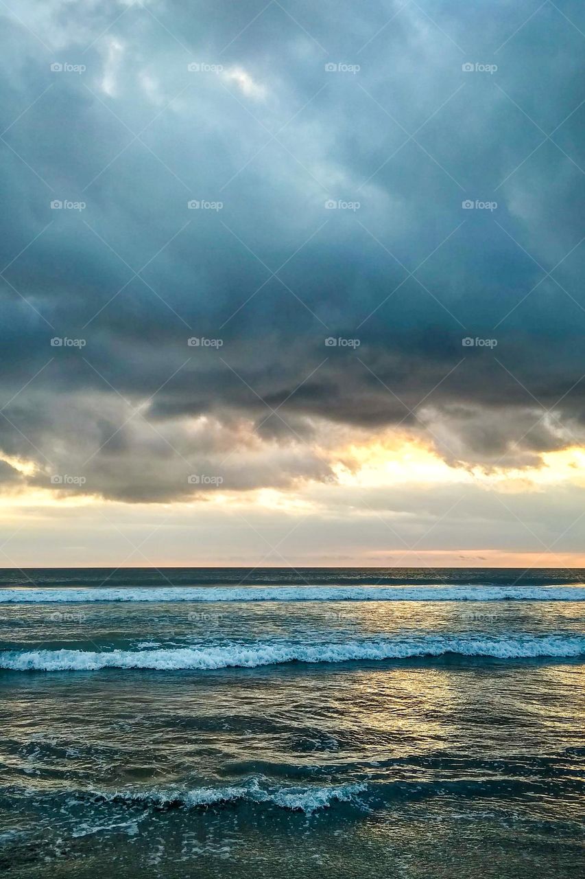 The beach is wavy and surrounded by clouds with the afternoon sun in an eye level view