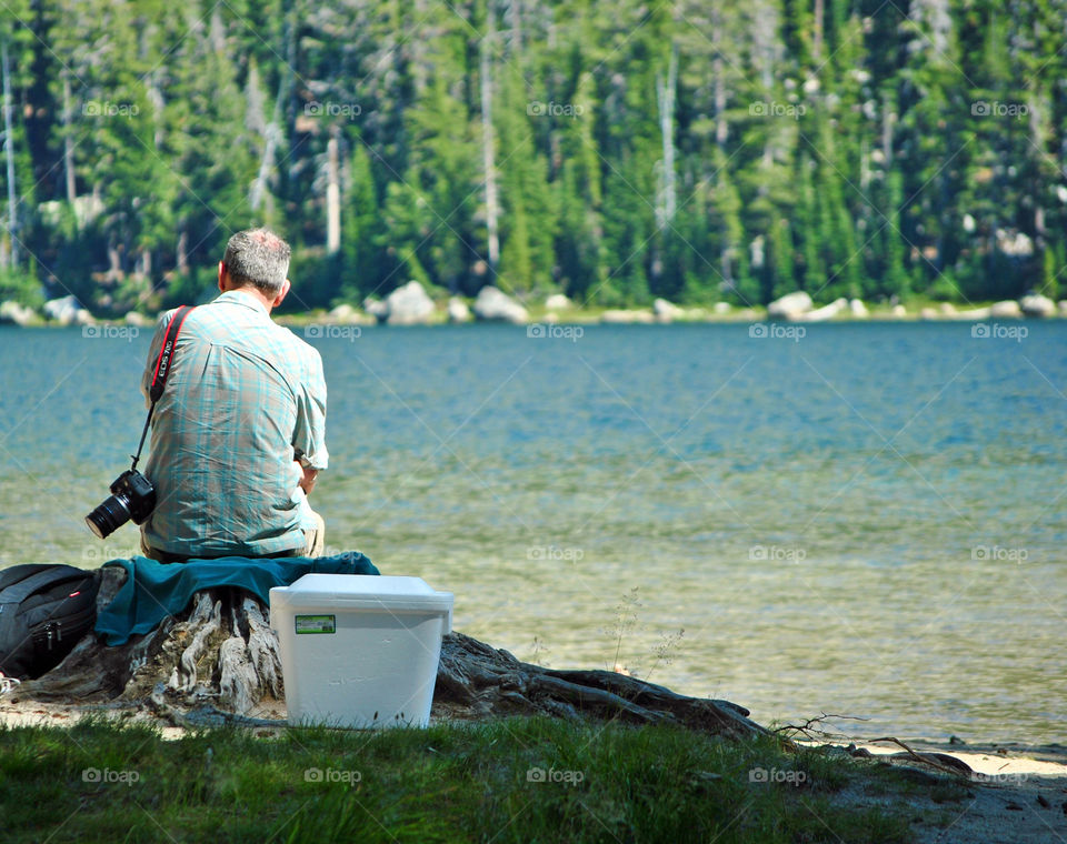 Old man carrying camera on his shoulder, sitting by the lake relaxing, elderly from behind