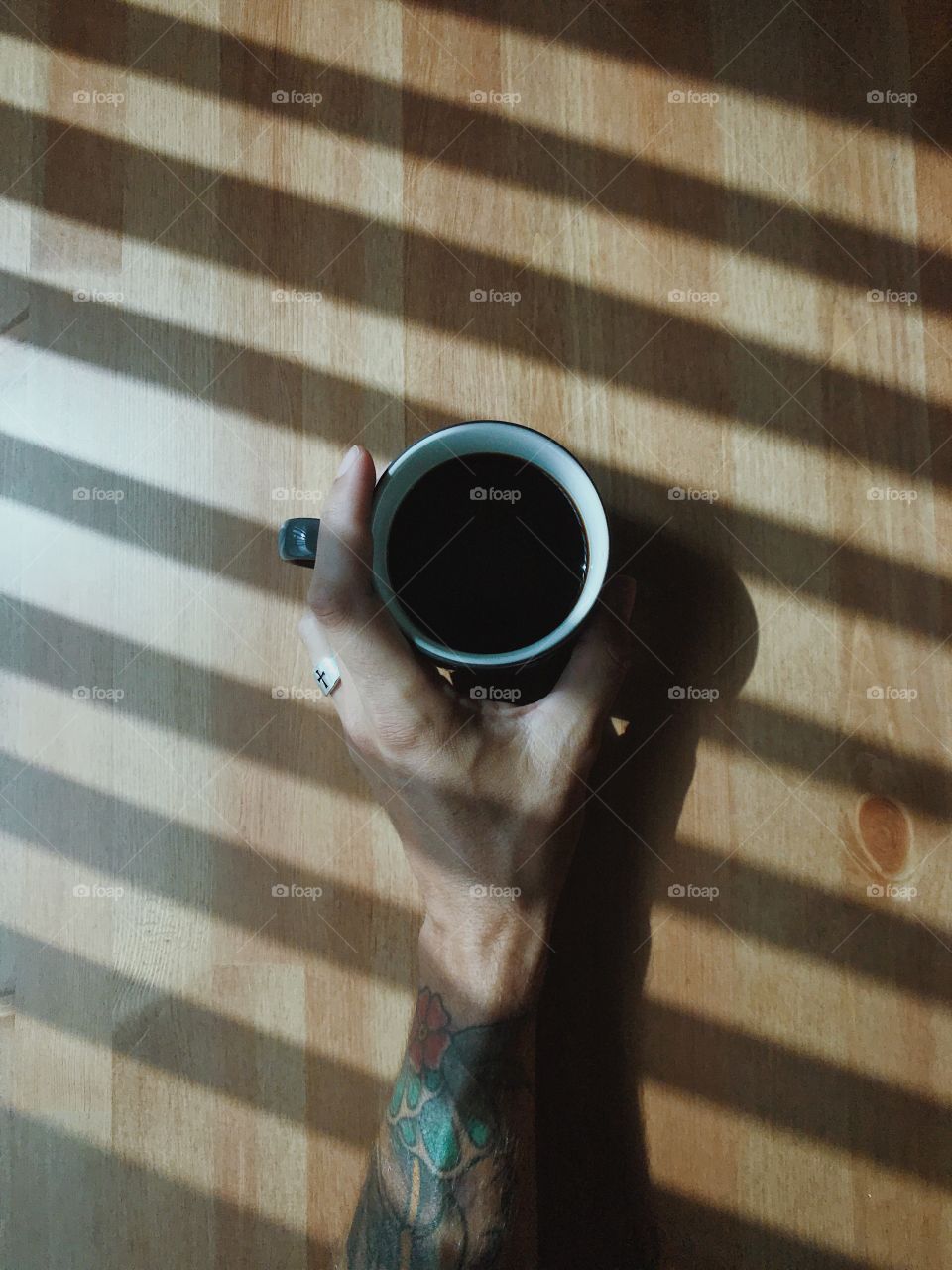 Man’s hand holding a coffee mug with window light creating interesting shadows.