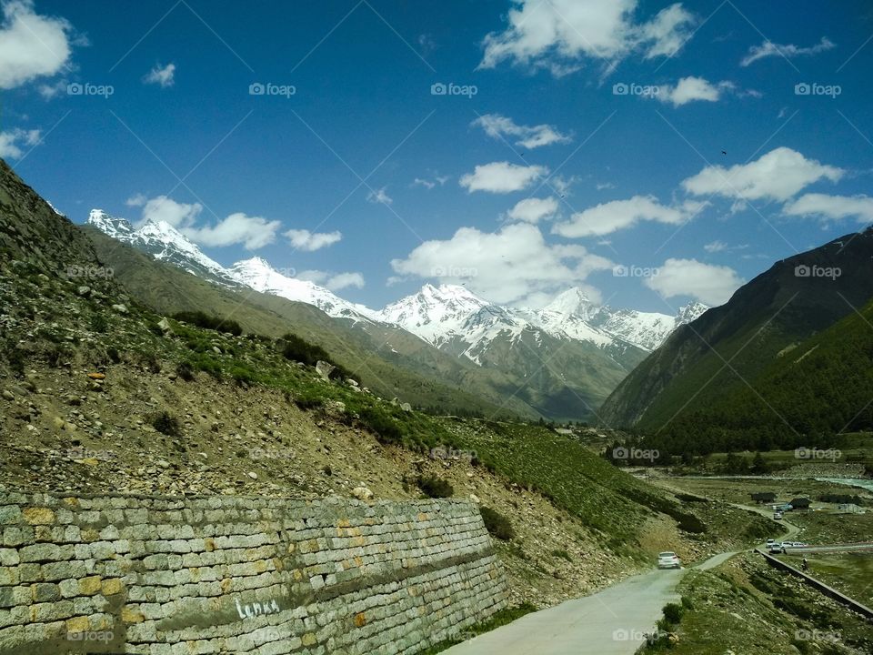 A Beautiful Shot of asphalt road to Baspa river in Chitkul village, Kinnaur valley, Himachal, India. A beautiful view of baspa river surrounded by green tree and snow capped mountains situated at chitkul village, Himachal, India.