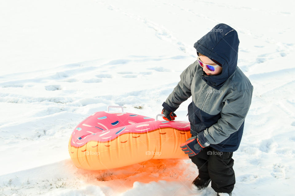 Young boy pulling a snow tube through the snow