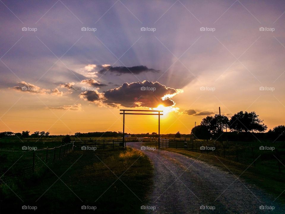 A country road  with the arch home at sunset with a cloud sunburst and purple sky in the evening