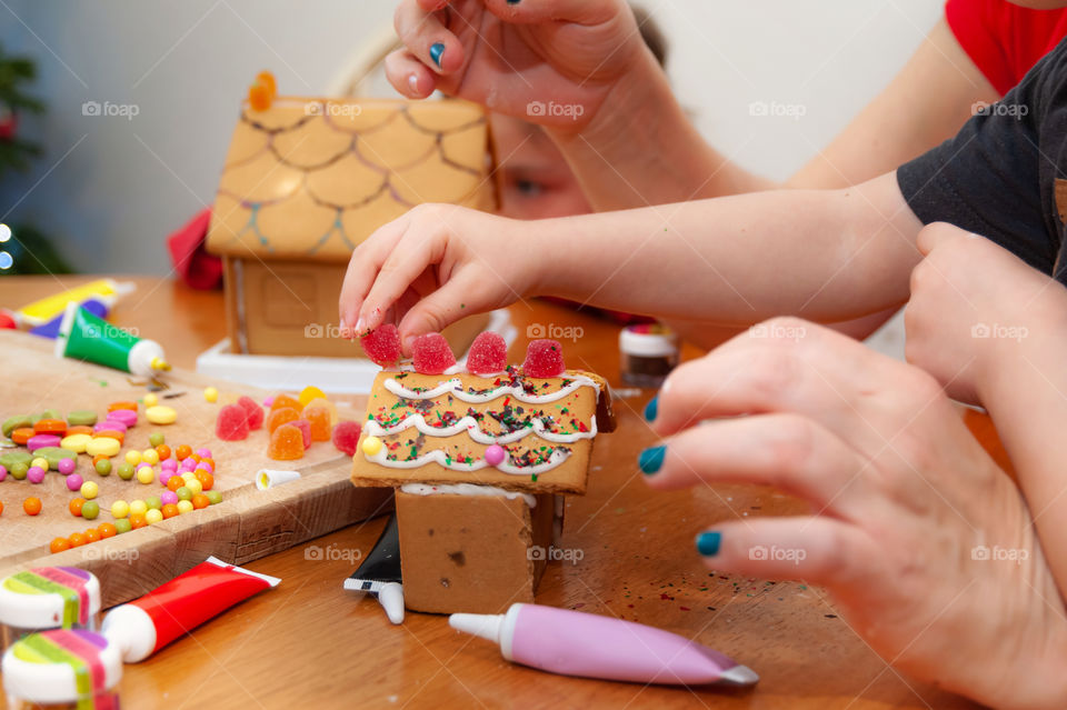 Children decorating gingerbread Christmas houses with colorful sweets and sparkling glitter.