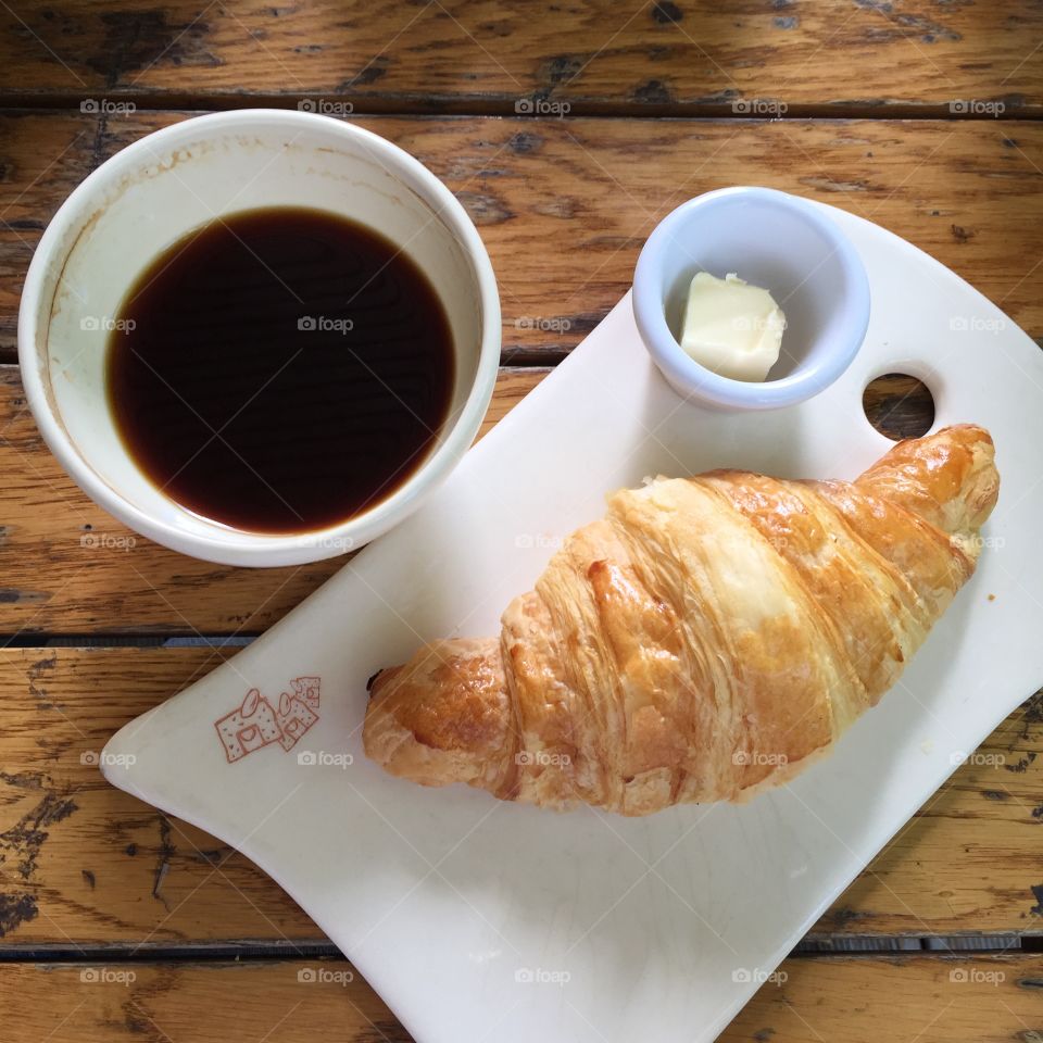French breakfast with black coffee and a croissant with butter.