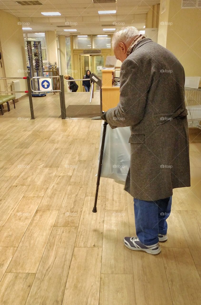 This old man just finish talking to a clerk at reception and checking something at his bag. 