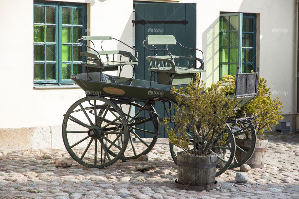 Old green carriage in front of a white house with green windows and door 