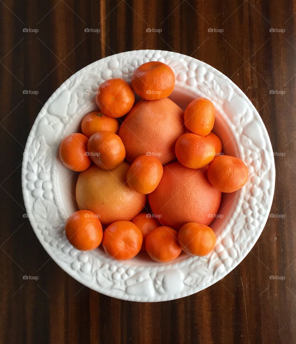 Oranges and clementines in a white fruit bowl on a wood surface