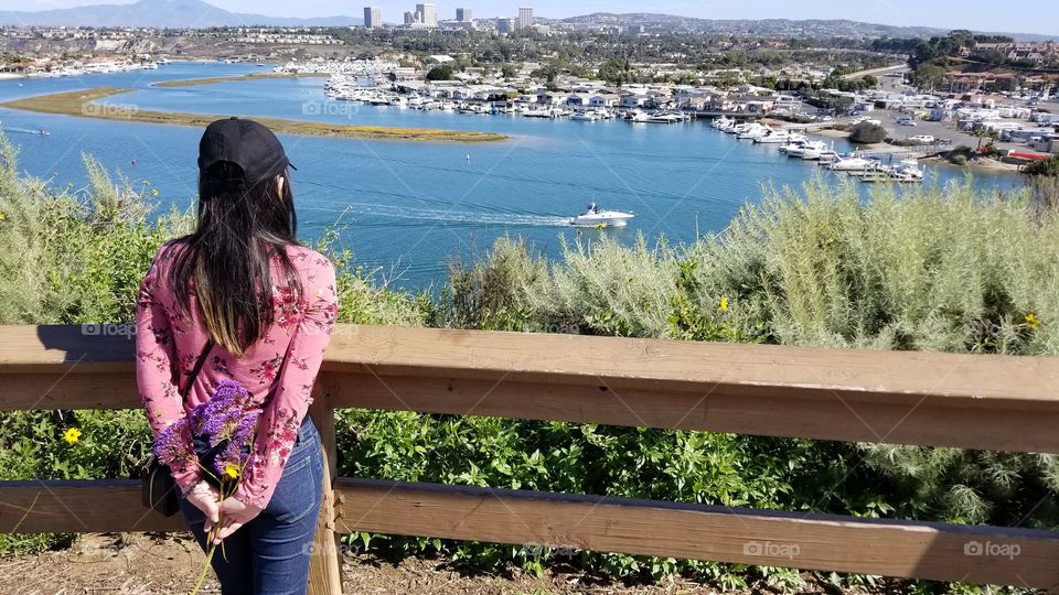fashionable woman holding a sea lavender flower on her back while looking at the beautiful view of the bay and the city