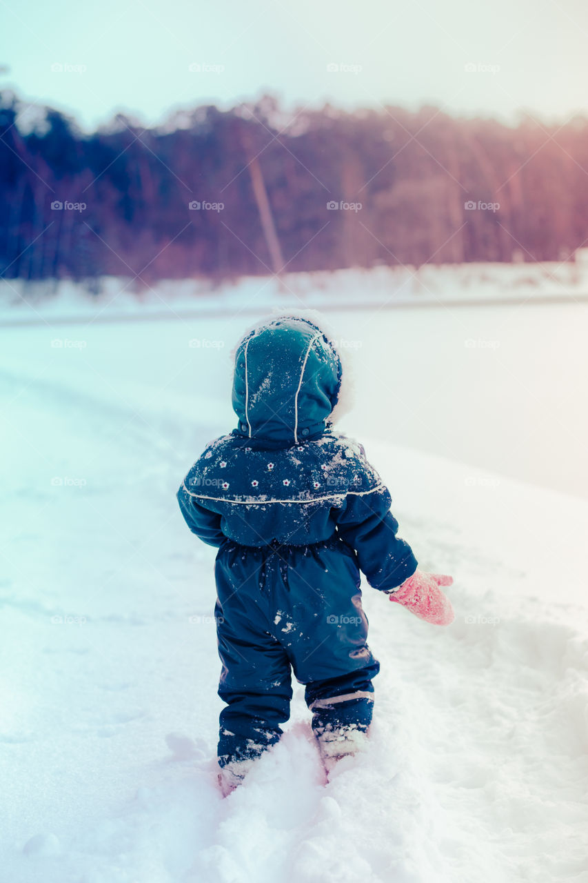 Little girl enjoying winter walking through deep snow. Toddler is playing outdoors while snow falling. Child is wearing dark blue snowsuit and wool cap