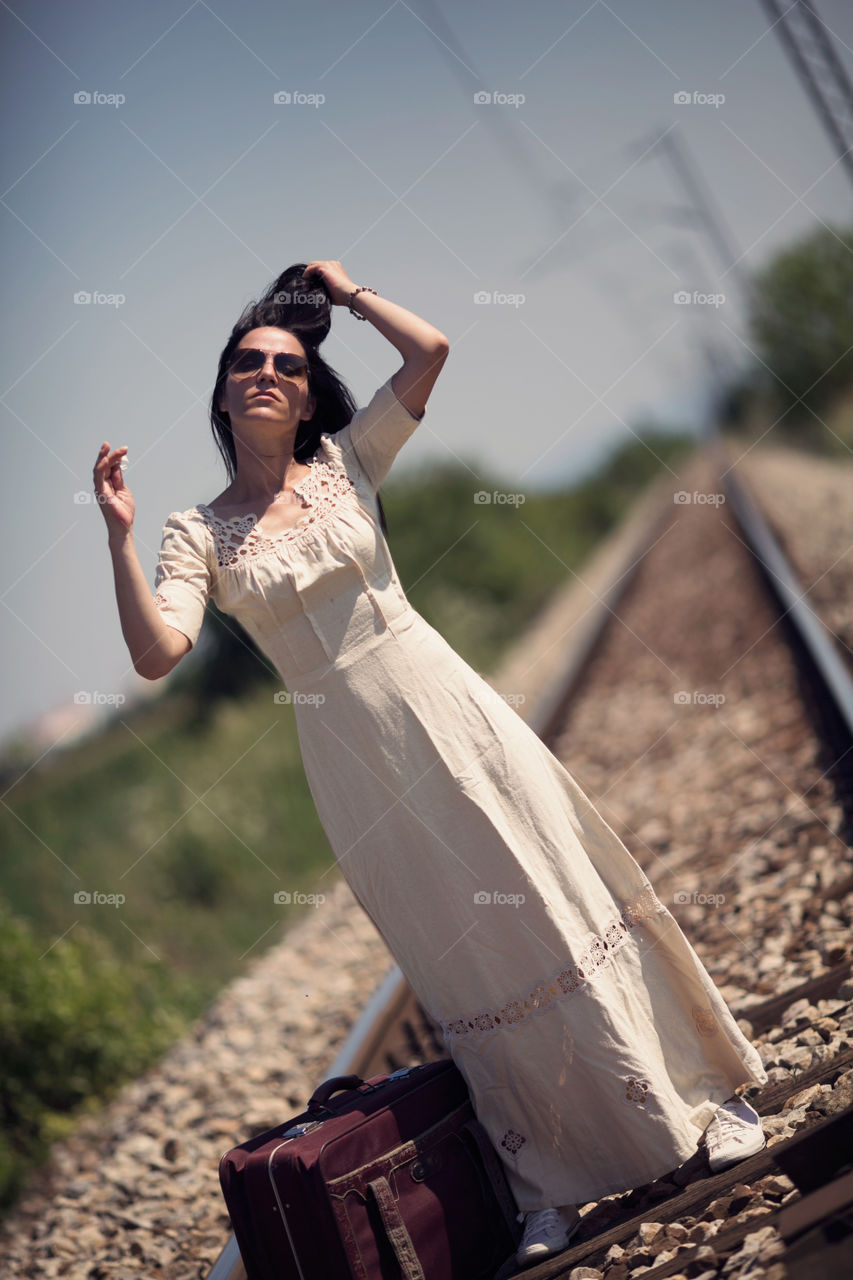 Young woman is posing with suitcase on the railway track