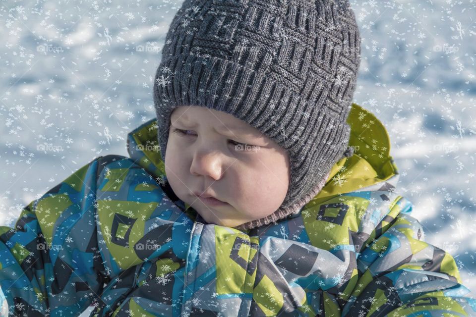 A child with a serious expression on his face in winter clothes jackets, pants, hat and boots in winter on the white snow on the street and in the park in nature plays winter fun.