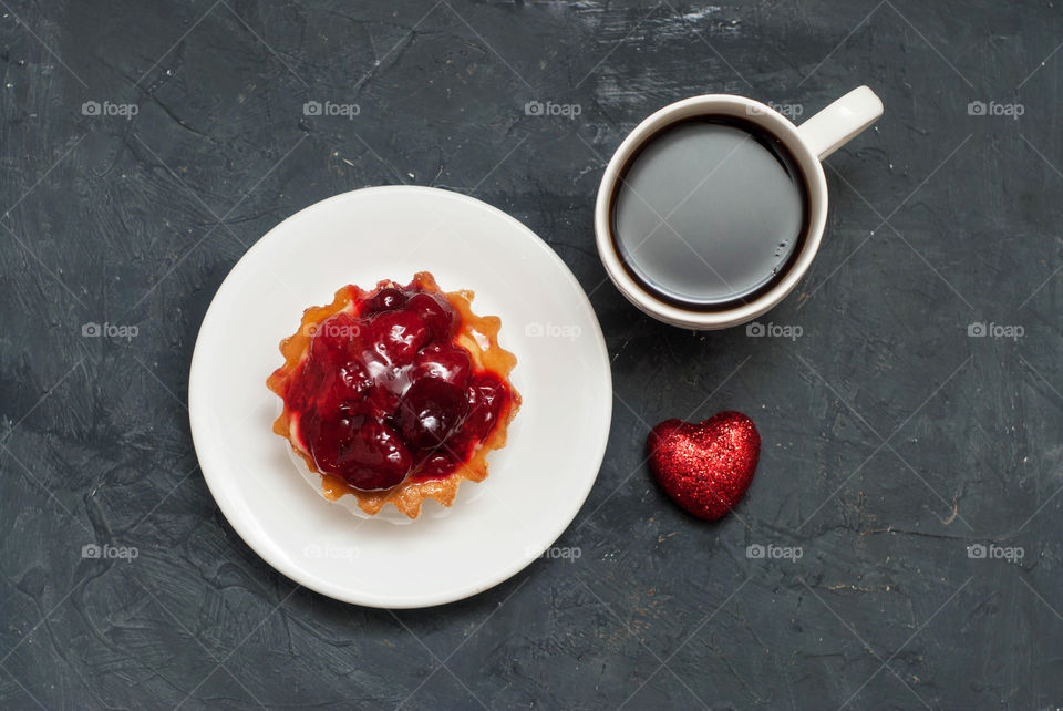 Fruit tarttlete cup of coffee and red heart. Breakfast with love concept. Textured dark background. Flat lay.