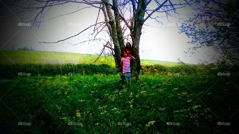 Two little girls standing next to a tree in a field on mountain.
