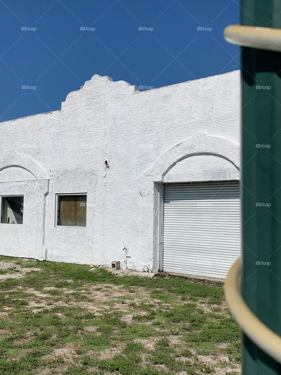 Old white architectural building with signs of aging elements under a blue sky in the afternoon with turned edges arched door and window with a peaking character on the left window.