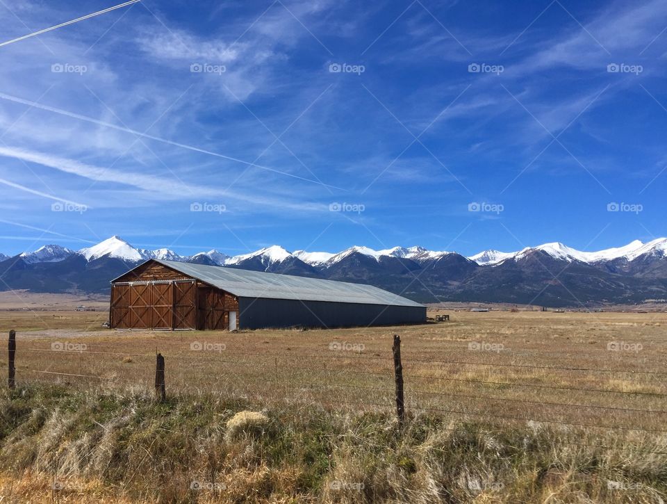 The beautiful snow topped Sangre de Cristo mountain range in Colorado, with a rustic barn in the foreground.
