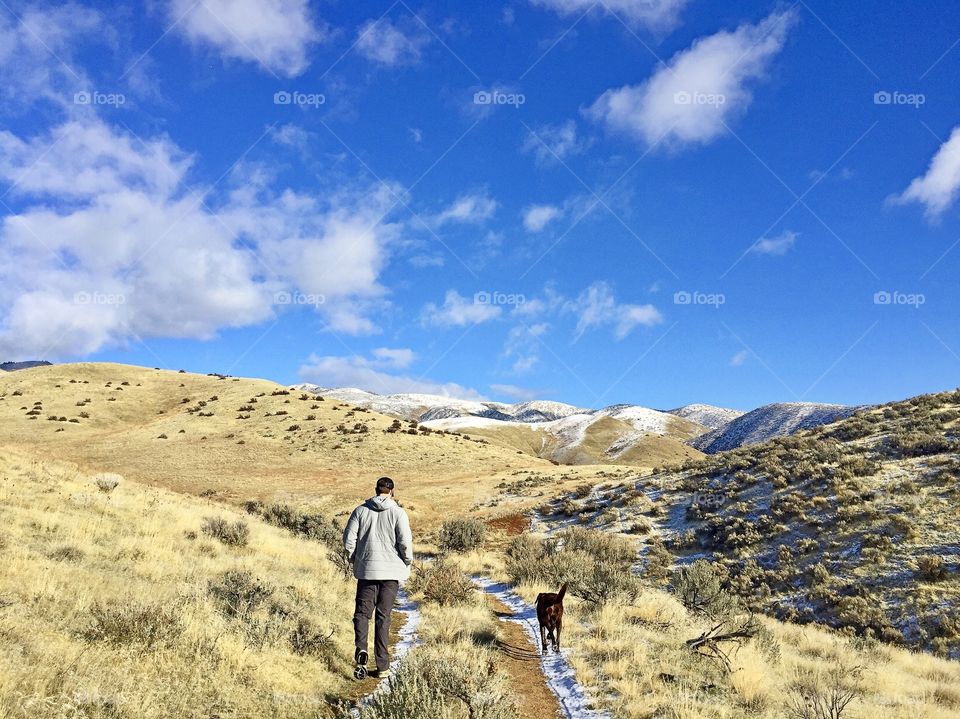 Man and his chocolate lab walking in the Boise foothills on a sunny spring day. 
