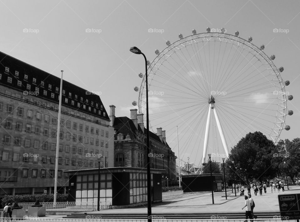 The London Eye towers above local historic buildings in London on a sunny summer day. 