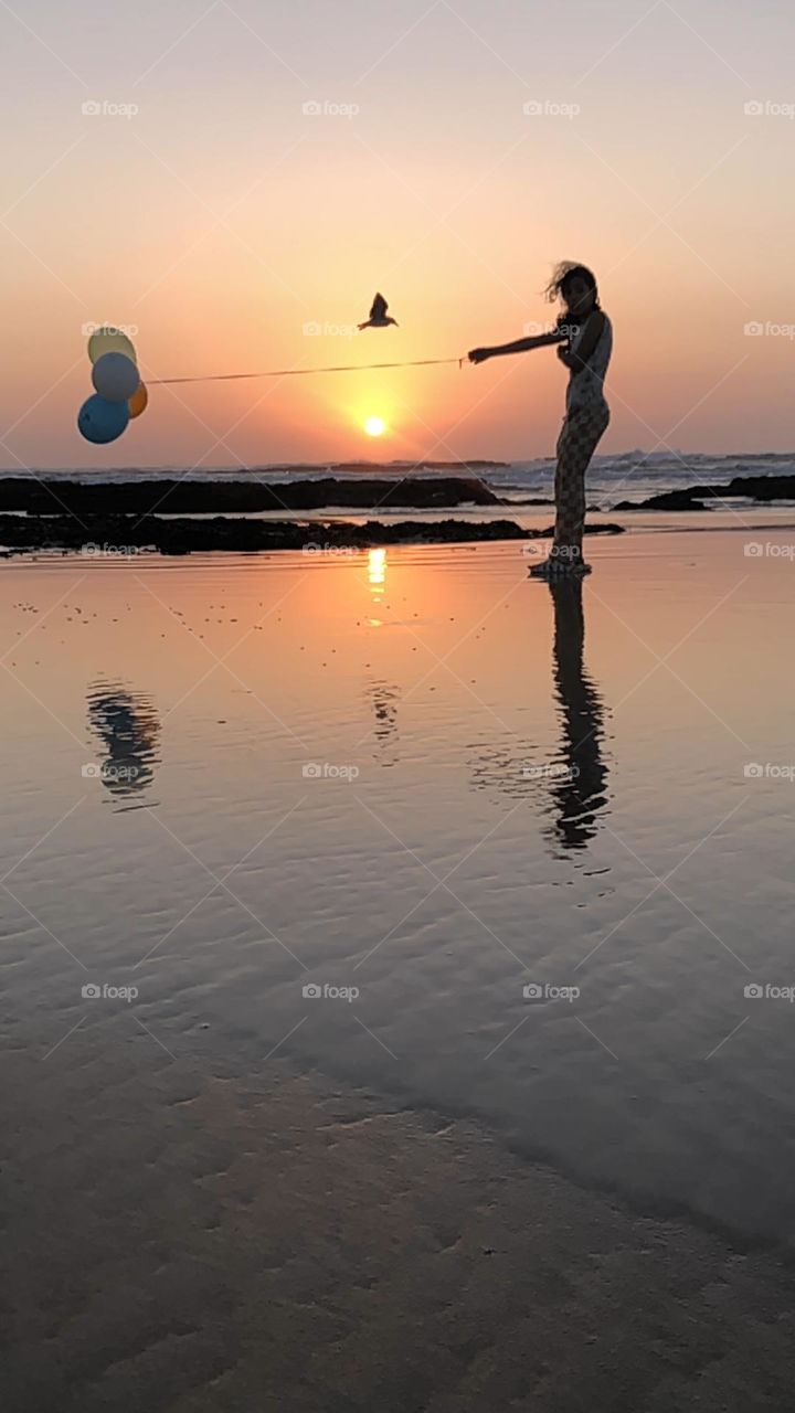 a young girl standing and holding multicolour balloons against splendid sunset at essaouira city in morocco.