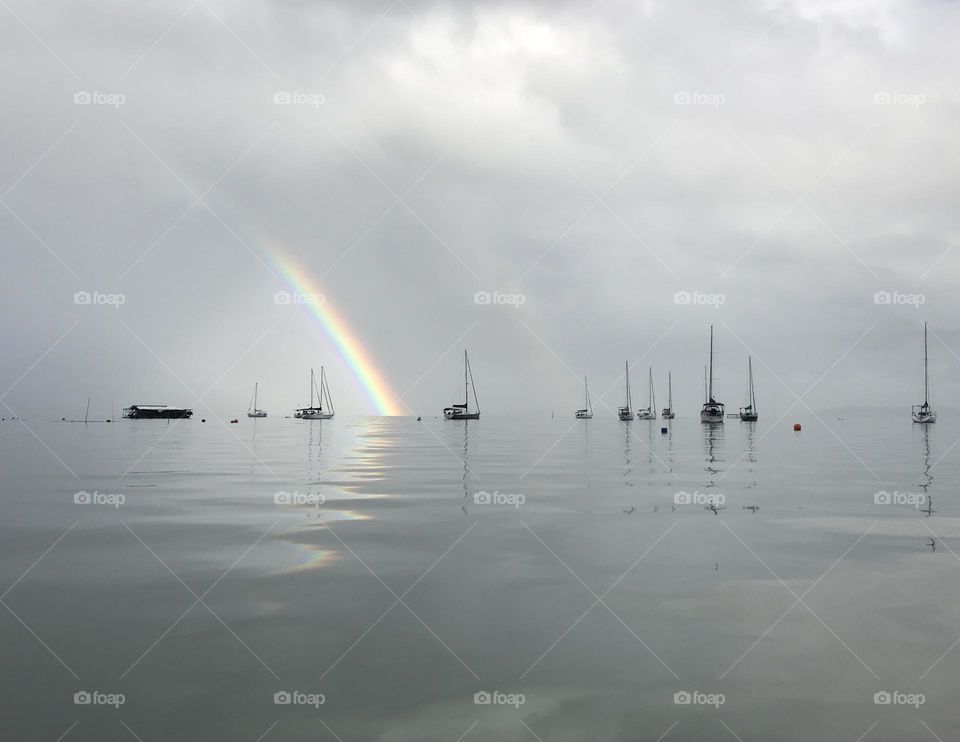 sailboats moored in Santo Antonio Bay, Florianópolis, Brazil, with a cloudy sky and rainbow