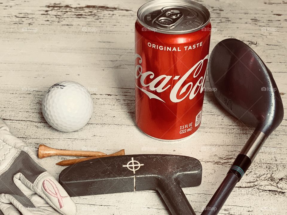 A can of Coca Cola and golf equipment on a rustic white background 